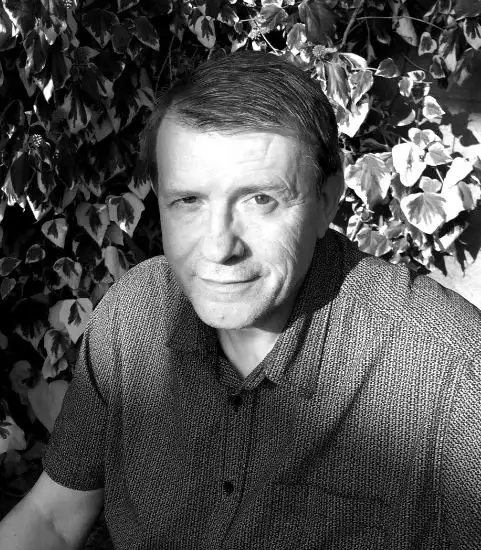 Black and white photo of crime author Tony Bassett sat with leaves behind him.